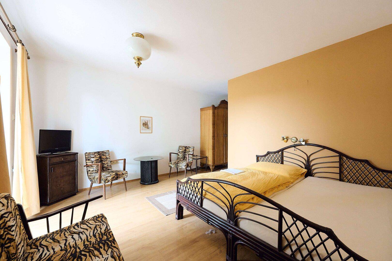 Geräumiges Schlafzimmer mit zwei Einzelbetten, Rattansesseln und einem Fernseher.