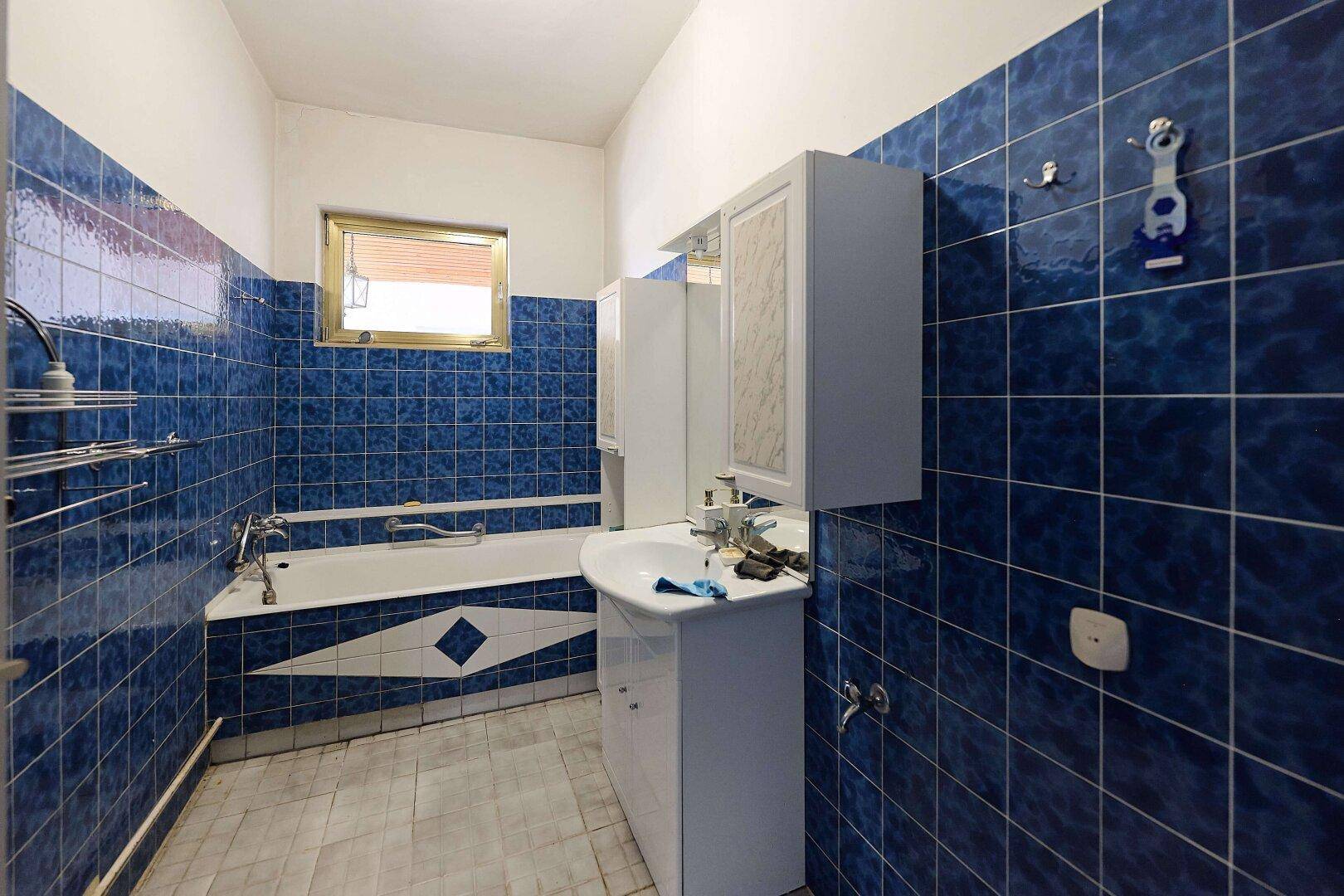 Badezimmer mit blauen Fliesen, Badewanne und einem Waschbecken mit Spiegelschrank.