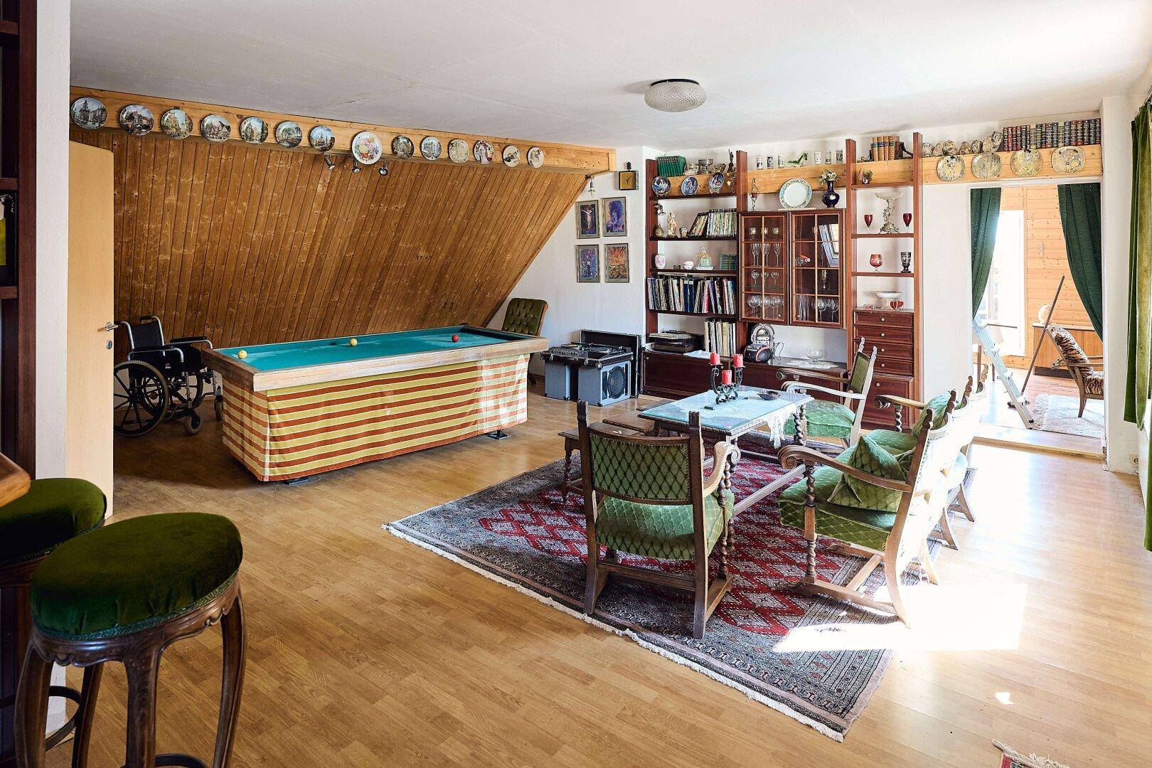 Geräumiger Dachbodenraum mit Billardtisch, Sitzgelegenheiten und Holzverkleidung.