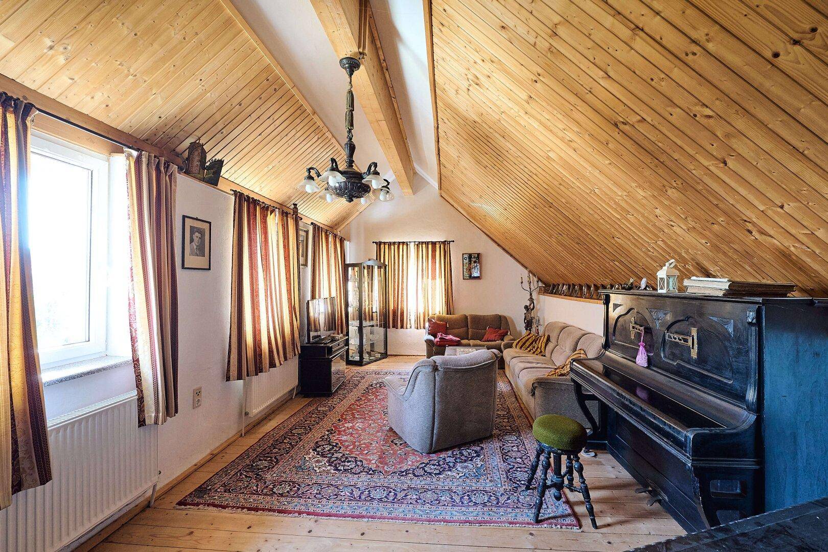 Gemütliches Wohnzimmer im Dachgeschoss mit Holzbalkendecke, Teppich und Klavier.