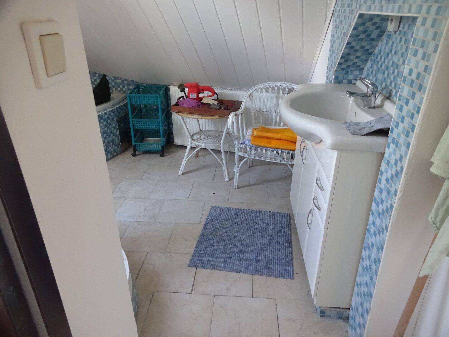 Badezimmer im Dachgeschoss mit Waschbecken, blauen Mosaikfliesen und schräger Decke.