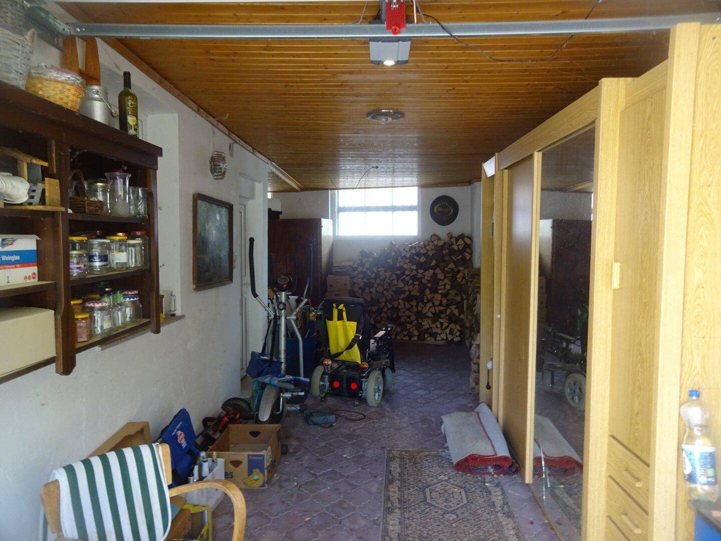 Abstellraum mit Holzdecke, Brennholzstapel und verschiedenen Lagergegenständen.