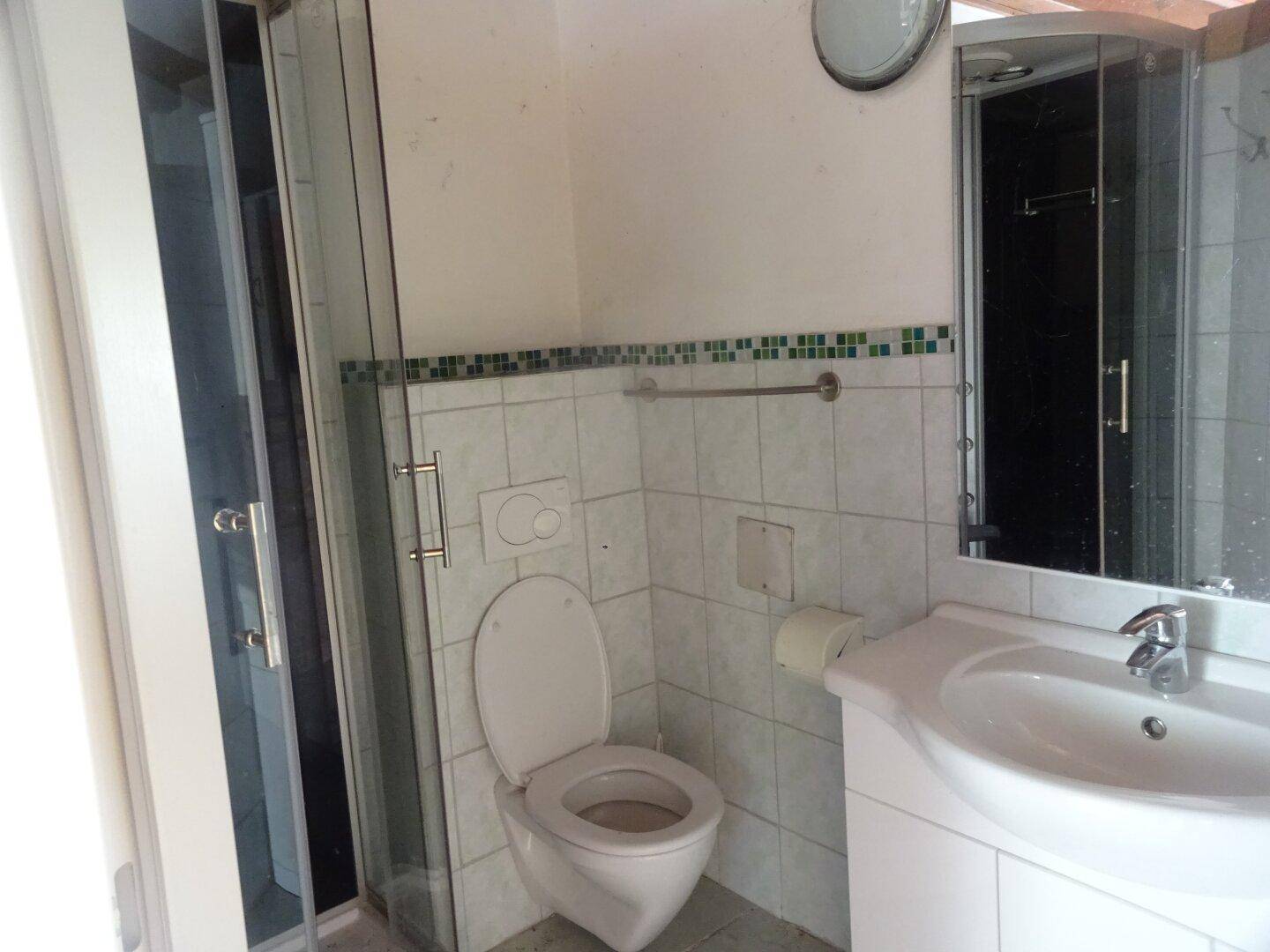 Badezimmer mit Duschkabine, WC und Waschbecken, ausgestattet mit weißen Fliesen und einem grünen Dekorstreifen.