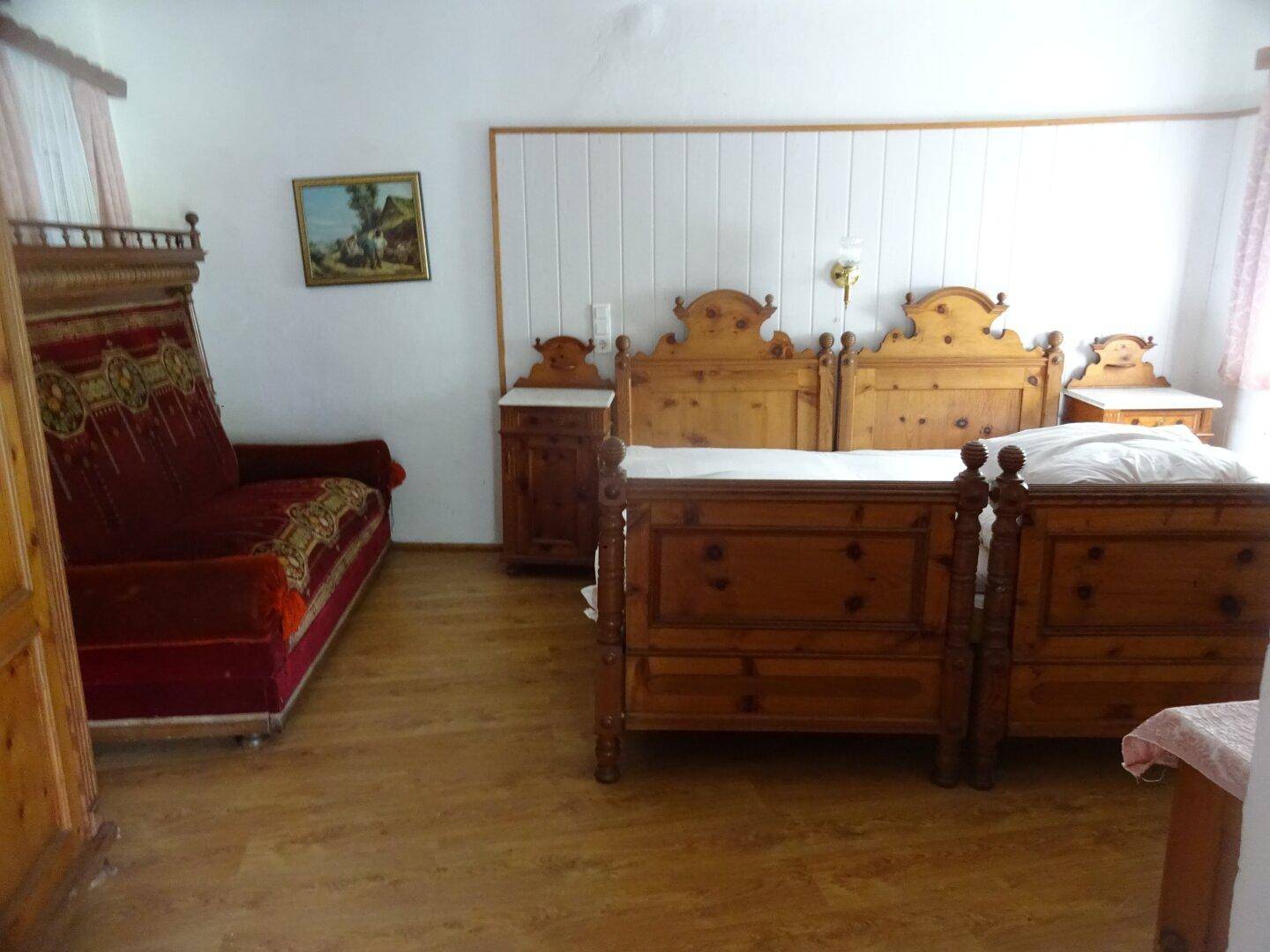 Schlafzimmer mit zwei traditionellen Holzbetten, einem roten Sofa und rustikalen Holzmöbeln.