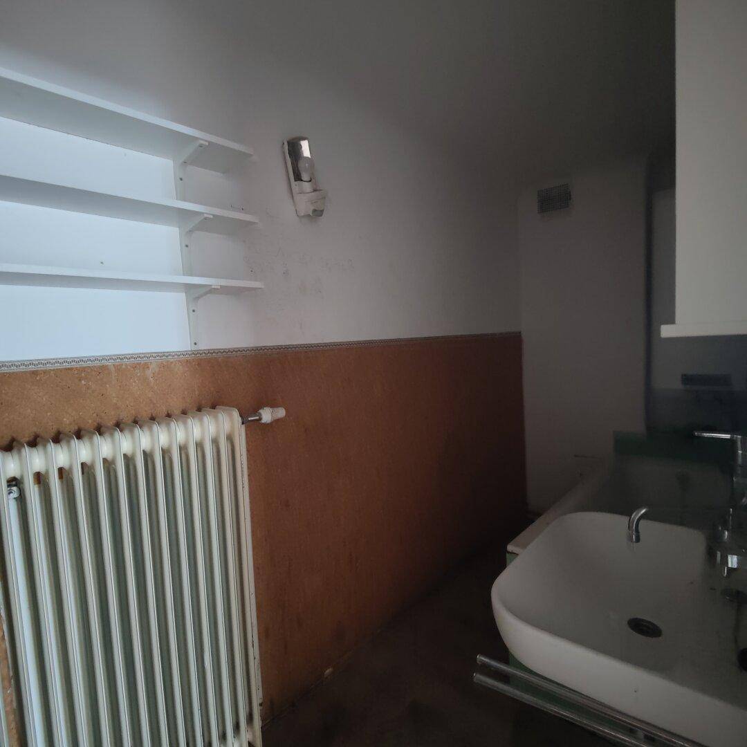 Kleiner, renovierungsbedürftiger Badezimmer- oder Hauswirtschaftsraum mit Waschbecken und Heizkörper.