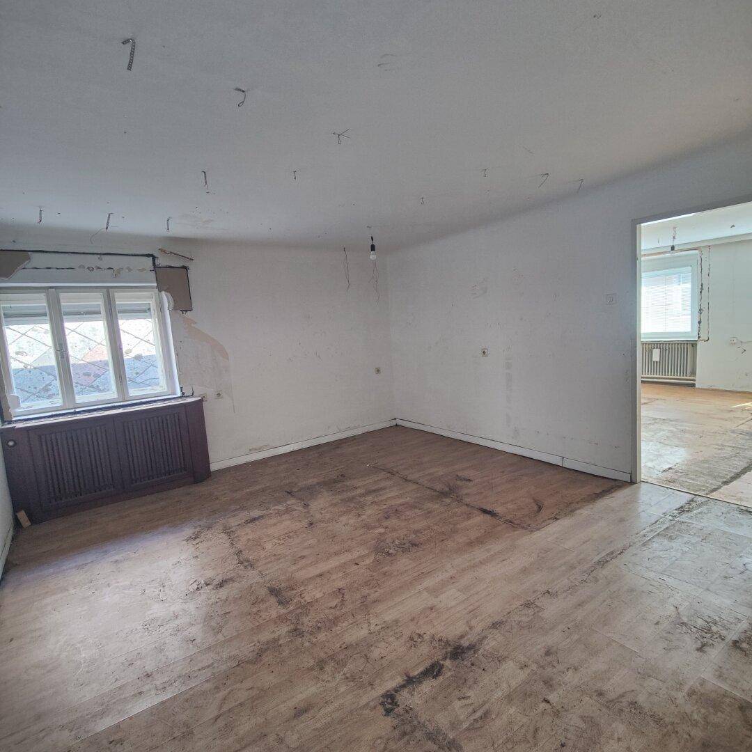 Leerer Raum mit Holzfußboden, einem Fenster und einem offenen Durchgang zu einem weiteren Zimmer.