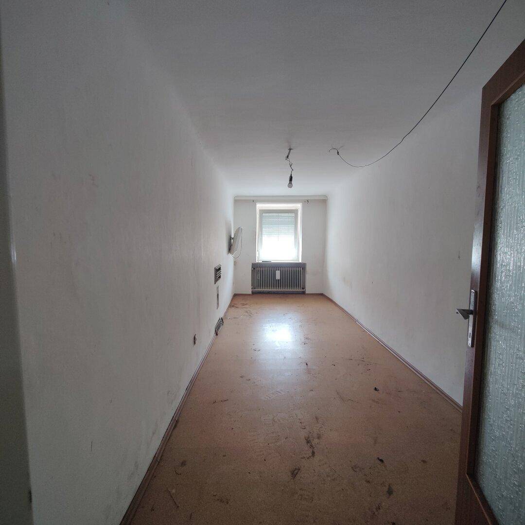 Schmaler, leerer Raum mit einem Fenster und Heizkörper, der auf Renovierung wartet.