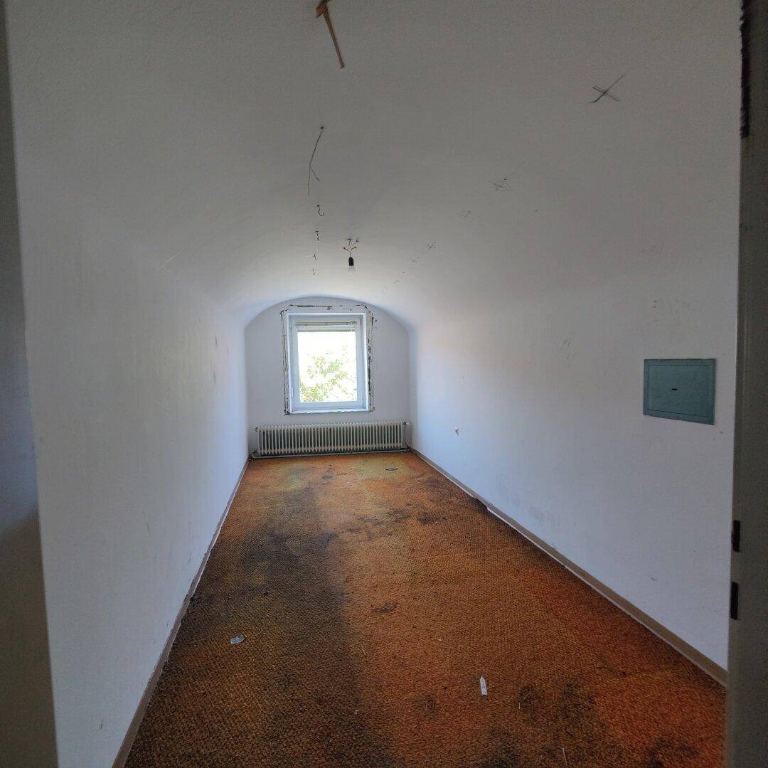Leerer Raum mit Gewölbedecke, Fenster und Heizkörper, der auf Renovierung wartet.