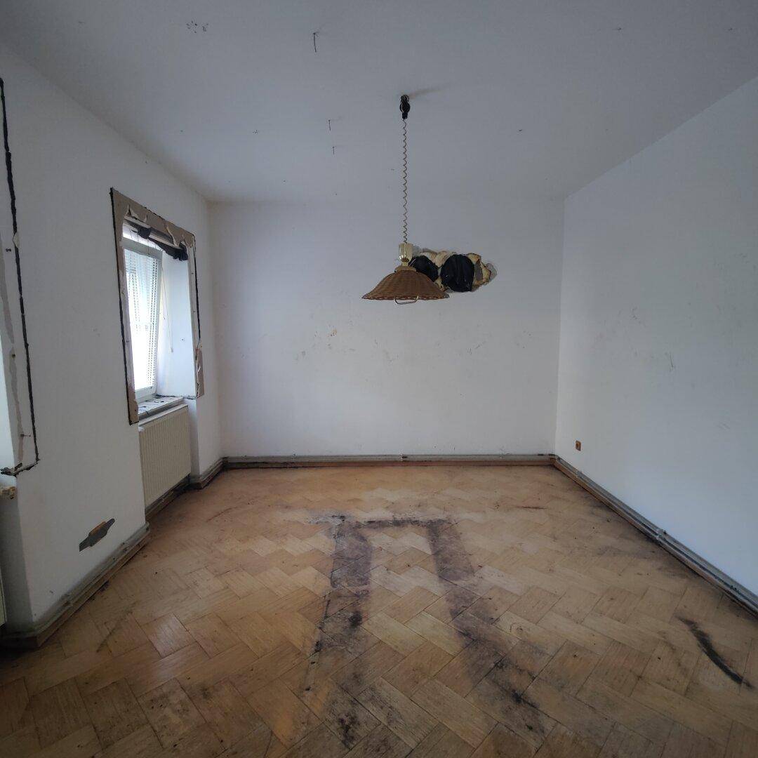 Leerer Raum mit altem Fischgrätparkettboden und einem Fenster, das Licht hereinlässt.