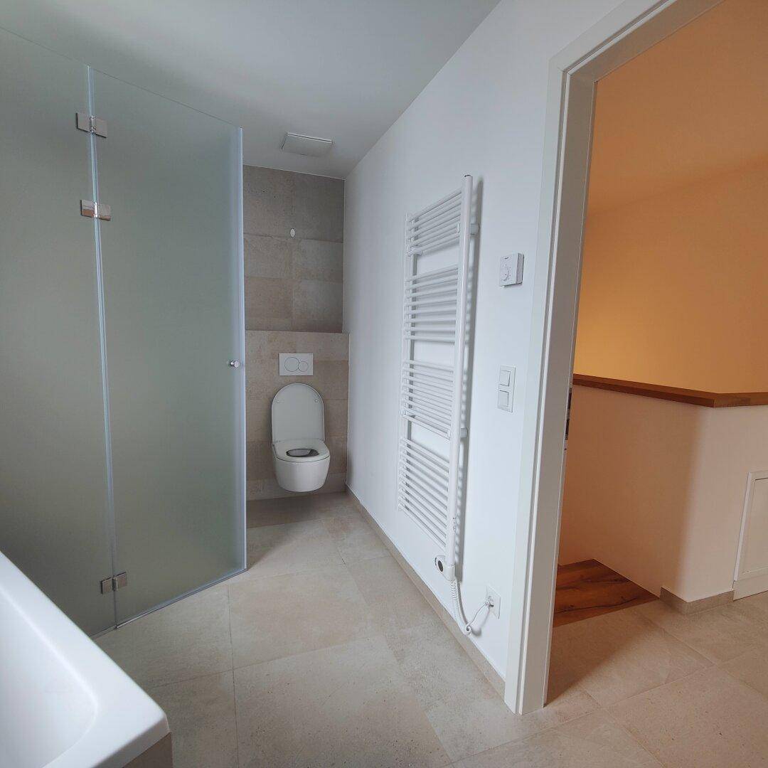 Modernes Badezimmer mit wandhängender Toilette, Duschkabine und beheiztem Handtuchhalter.