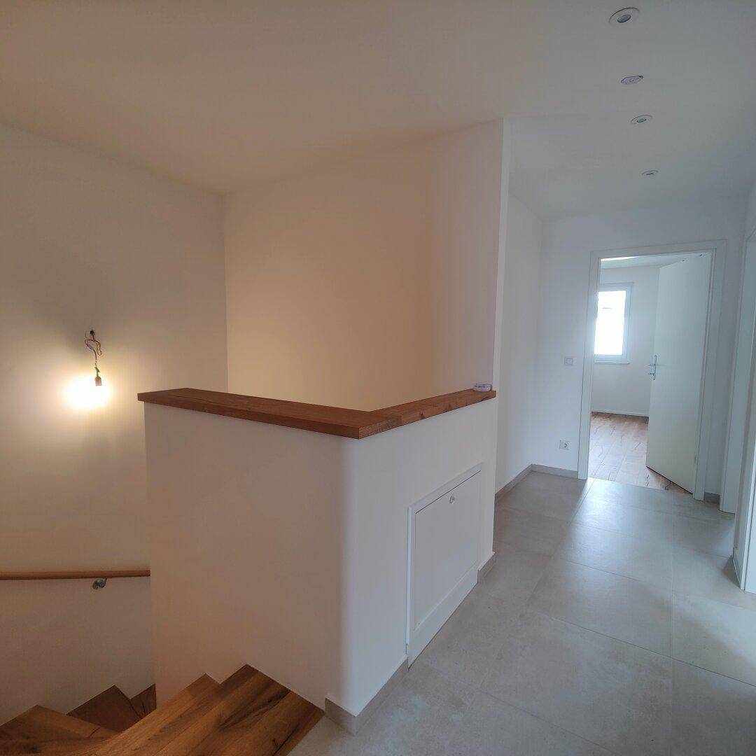 Heller Treppenabsatz mit Holztreppe, Fliesenboden und integrierten Deckenspots.