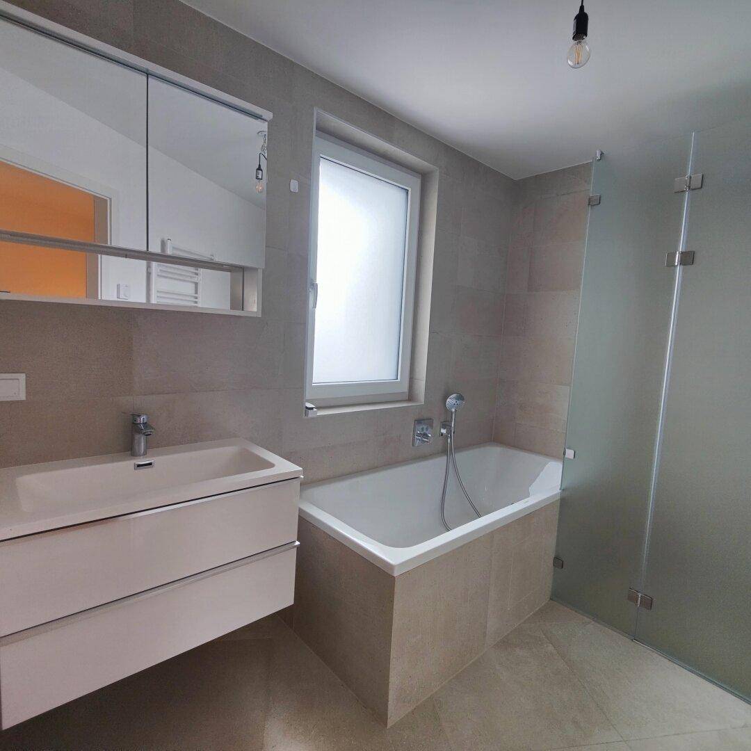 Modernes Badezimmer mit Badewanne, Doppelwaschbecken, Duschkabine und Fenster.