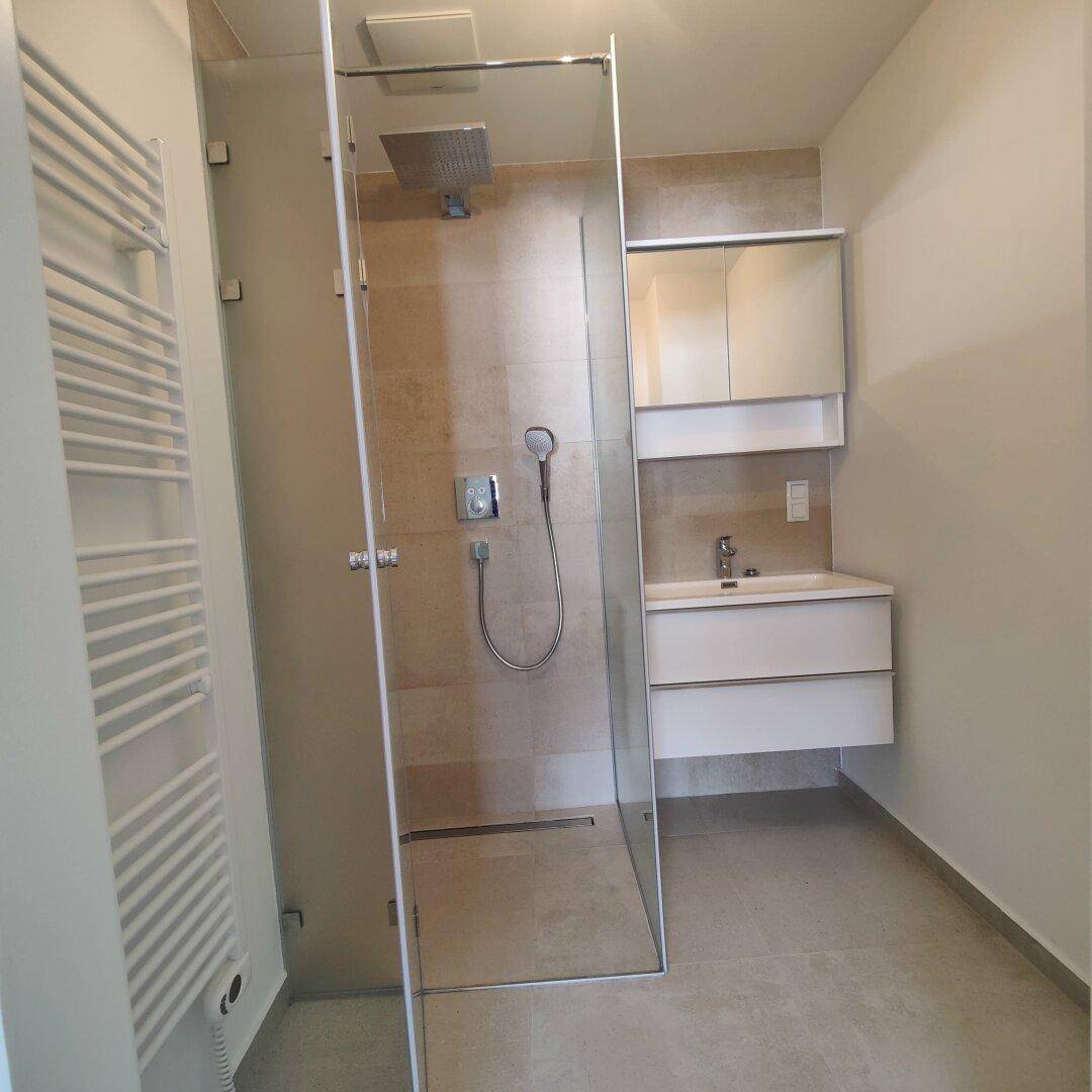 Modernes Badezimmer mit ebenerdiger Dusche, Waschbecken und beheiztem Handtuchhalter.