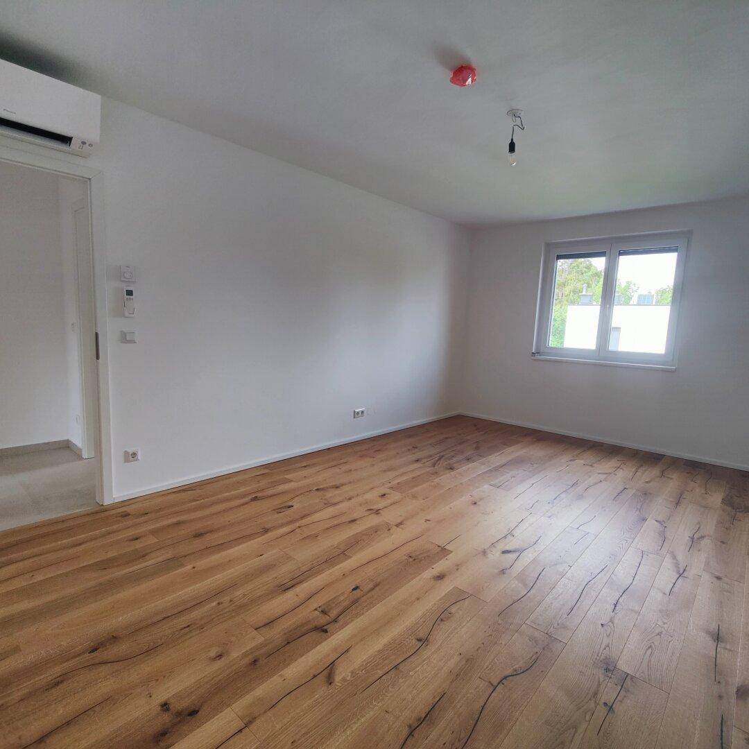 Helles Schlafzimmer mit Holzboden und großem Fenster, das viel Tageslicht hereinlässt.