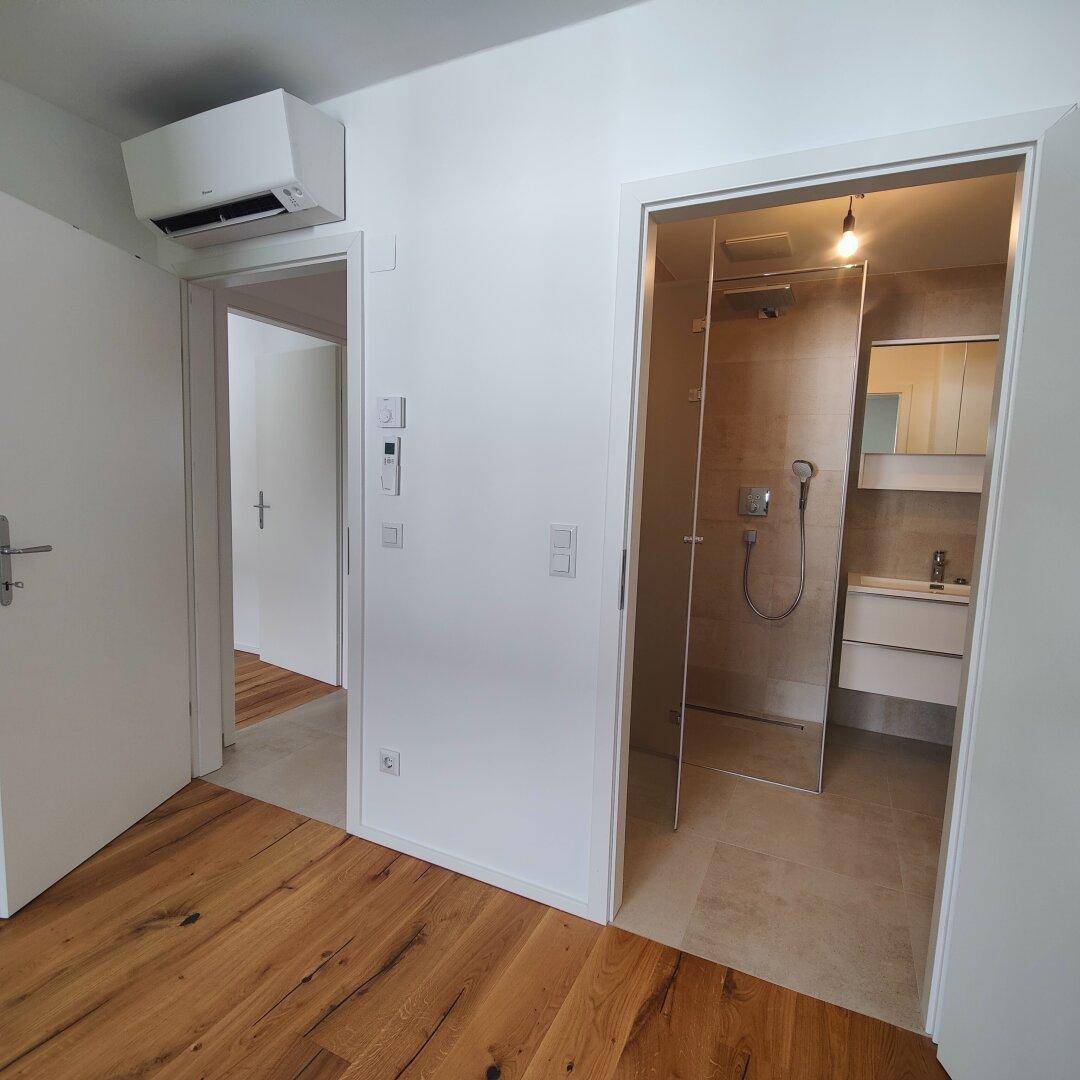 Schlafzimmer mit Holzboden und Klimaanlage, direkter Zugang zu einem modernen Badezimmer.
