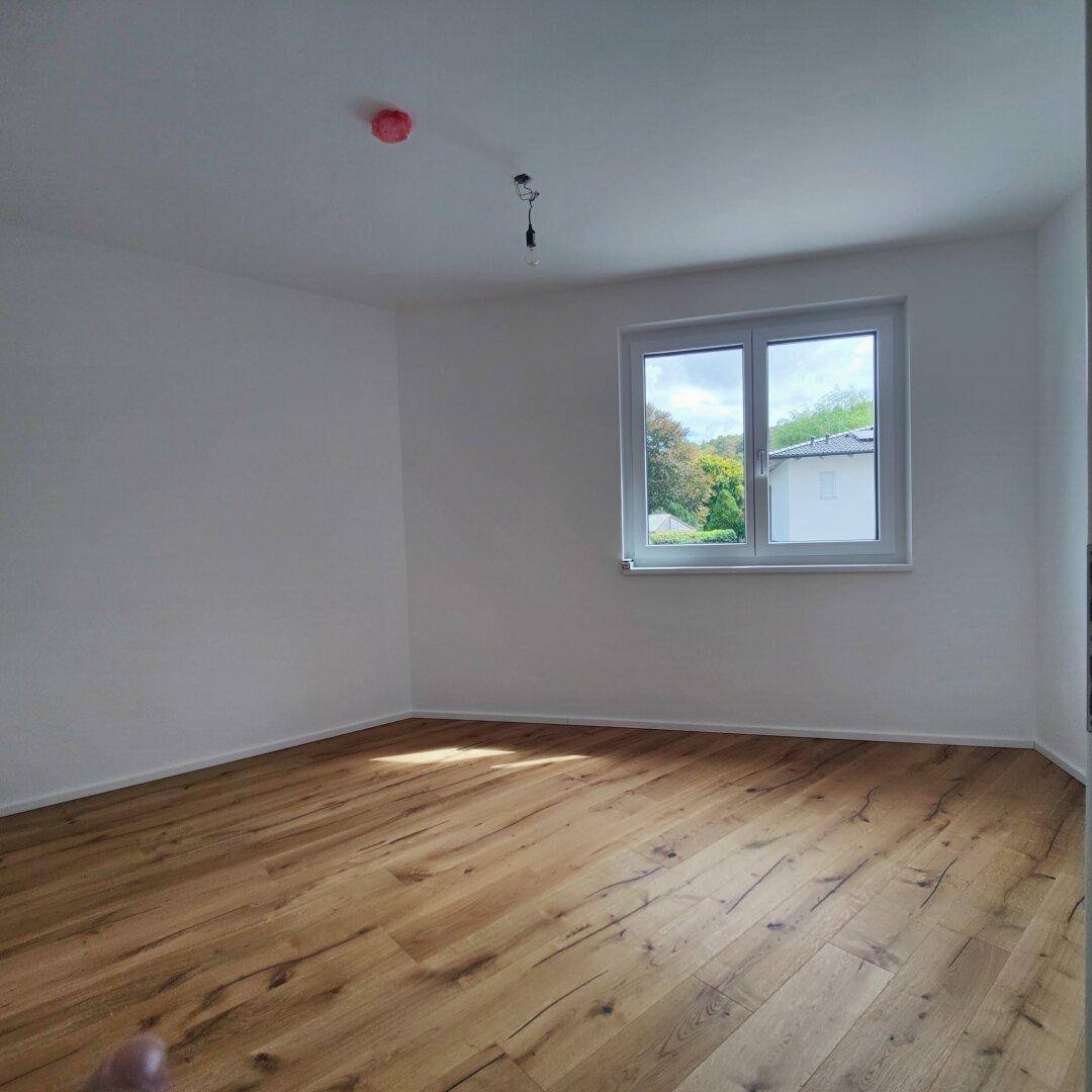 Geräumiges Schlafzimmer mit Holzboden und Fenster, das einen Blick ins Grüne bietet.