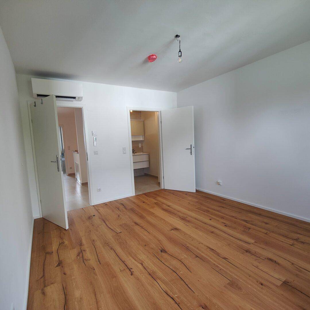 Helles Schlafzimmer mit Holzboden und Klimaanlage, mit Zugang zu einem angrenzenden Badezimmer.