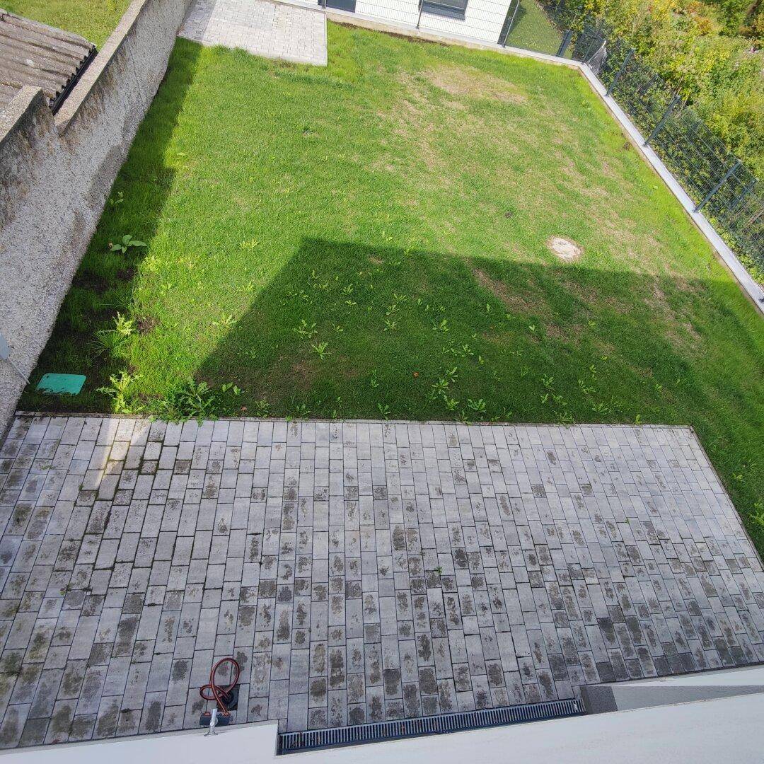 Große gepflasterte Terrasse mit angrenzendem Rasenbereich und Blick ins Grüne.