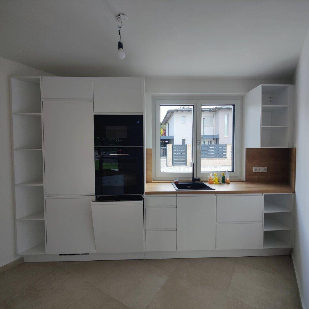Helle Einbauküche mit weißen Schränken, Holzdetails und Fenster mit Blick nach draußen.