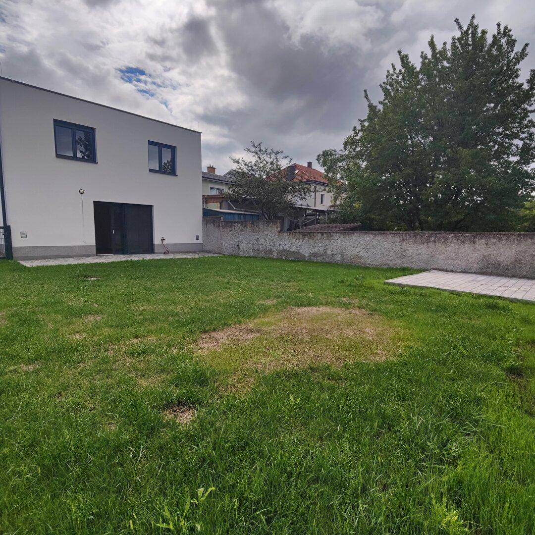 Großer Gartenbereich hinter dem Haus mit Rasenfläche und einer Steinmauer.