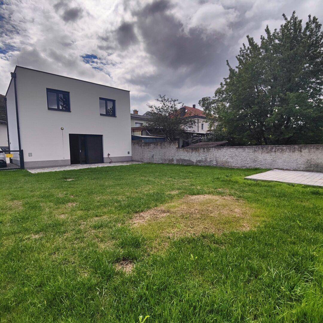 Weitläufiger Garten mit Rasenfläche und Blick auf die Rückseite des modernen Neubaus.