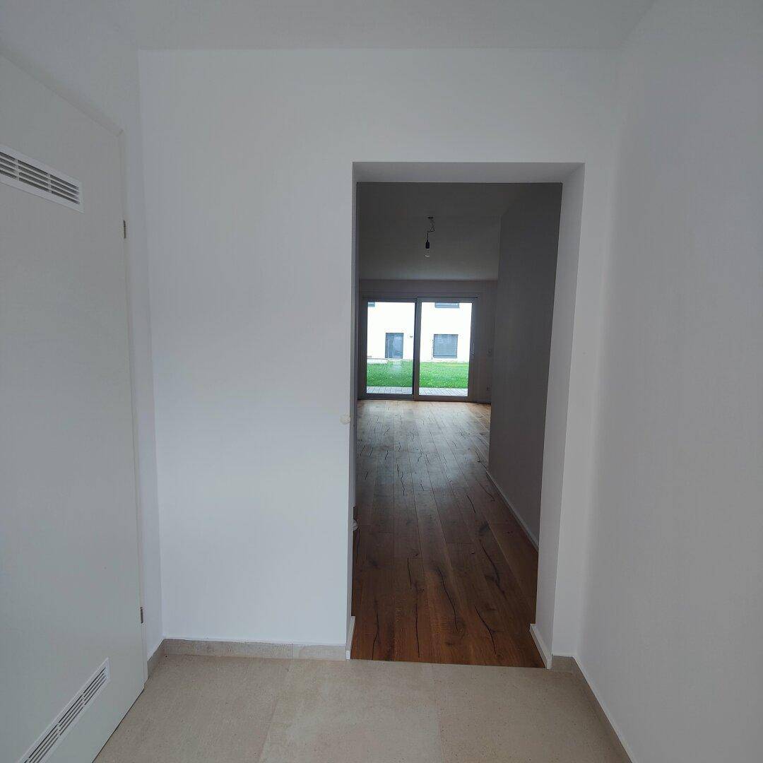 Heller Flur mit Fliesenboden, der zu einem Wohnbereich mit Holzboden und Terrassenzugang führt.
