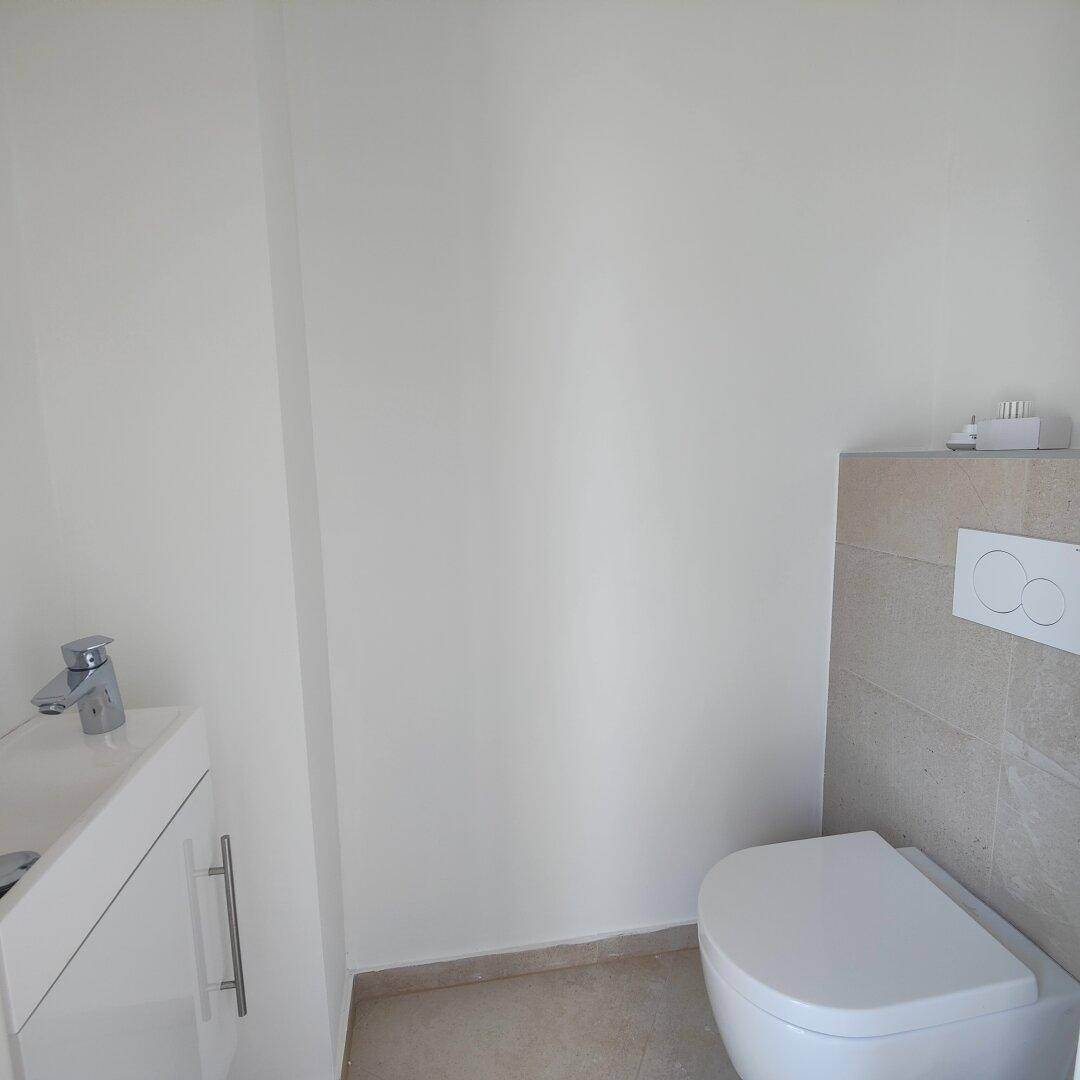 Modernes Gäste-WC mit wandhängender Toilette, kleinem Waschbecken und hellen Fliesen.