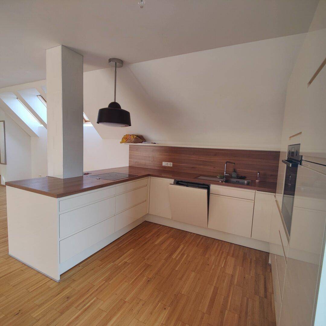 Moderne Einbauküche mit weißen Schränken, Holz-Arbeitsplatten und integrierten Geräten unter einer Dachschräge.
