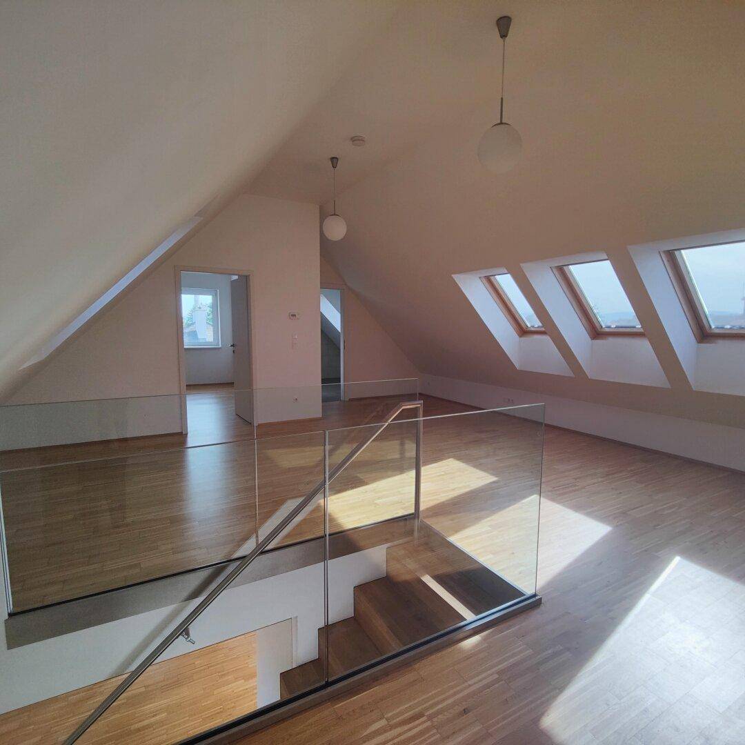 Offener Dachgeschossbereich mit Holzboden, Dachschrägen, Dachfenstern und einer modernen Glasbrüstung.