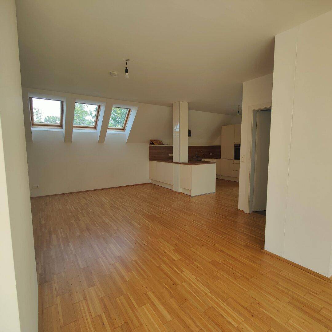 Offener Wohnbereich mit Holzboden, Dachschrägen und mehreren Dachfenstern, die viel Licht hereinlassen.