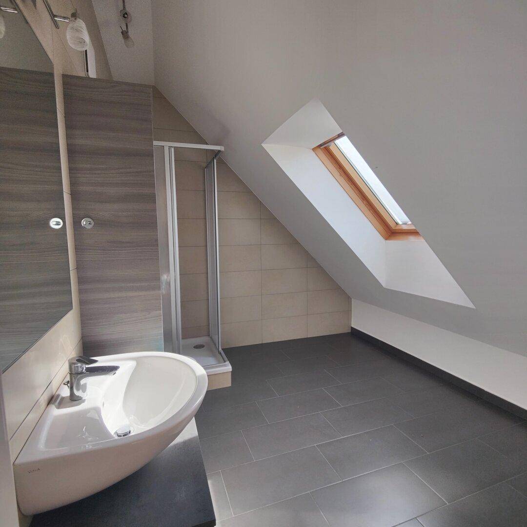 Modernes Badezimmer im Dachgeschoss mit Duschkabine, Waschbecken und einem Dachfenster für natürliches Licht.