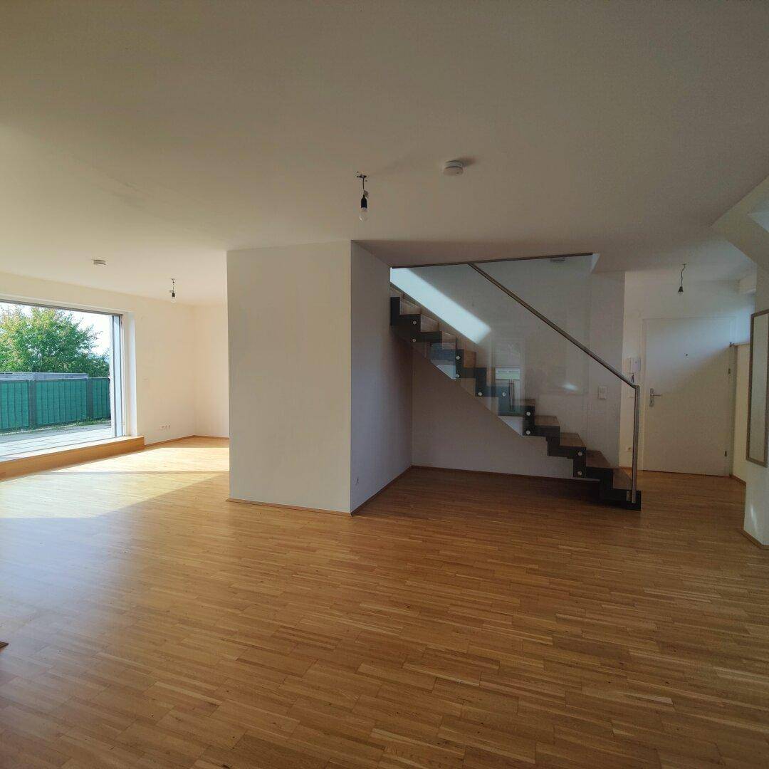 Geräumiges Wohnzimmer mit Holzboden, moderner Glastreppe und großem Fenster mit Zugang zur Terrasse.