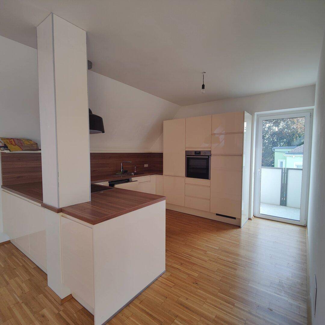 Helle Küche mit weißen Schränken, Holz-Arbeitsplatten und direktem Zugang zu einem Balkon oder einer Terrasse.