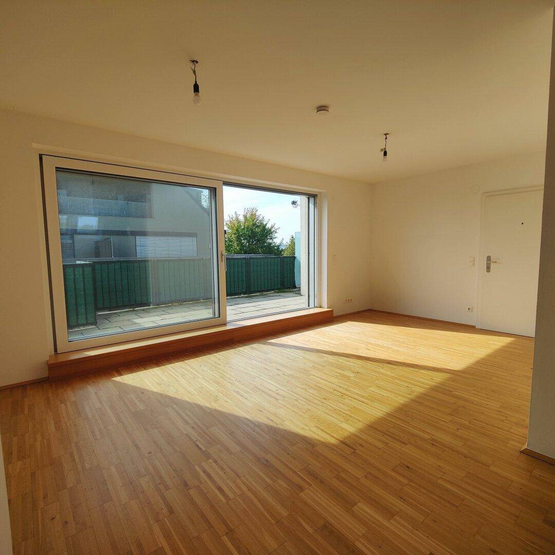 Sonniges Wohnzimmer mit Holzboden und großer Schiebetür, die auf eine geräumige Terrasse führt.