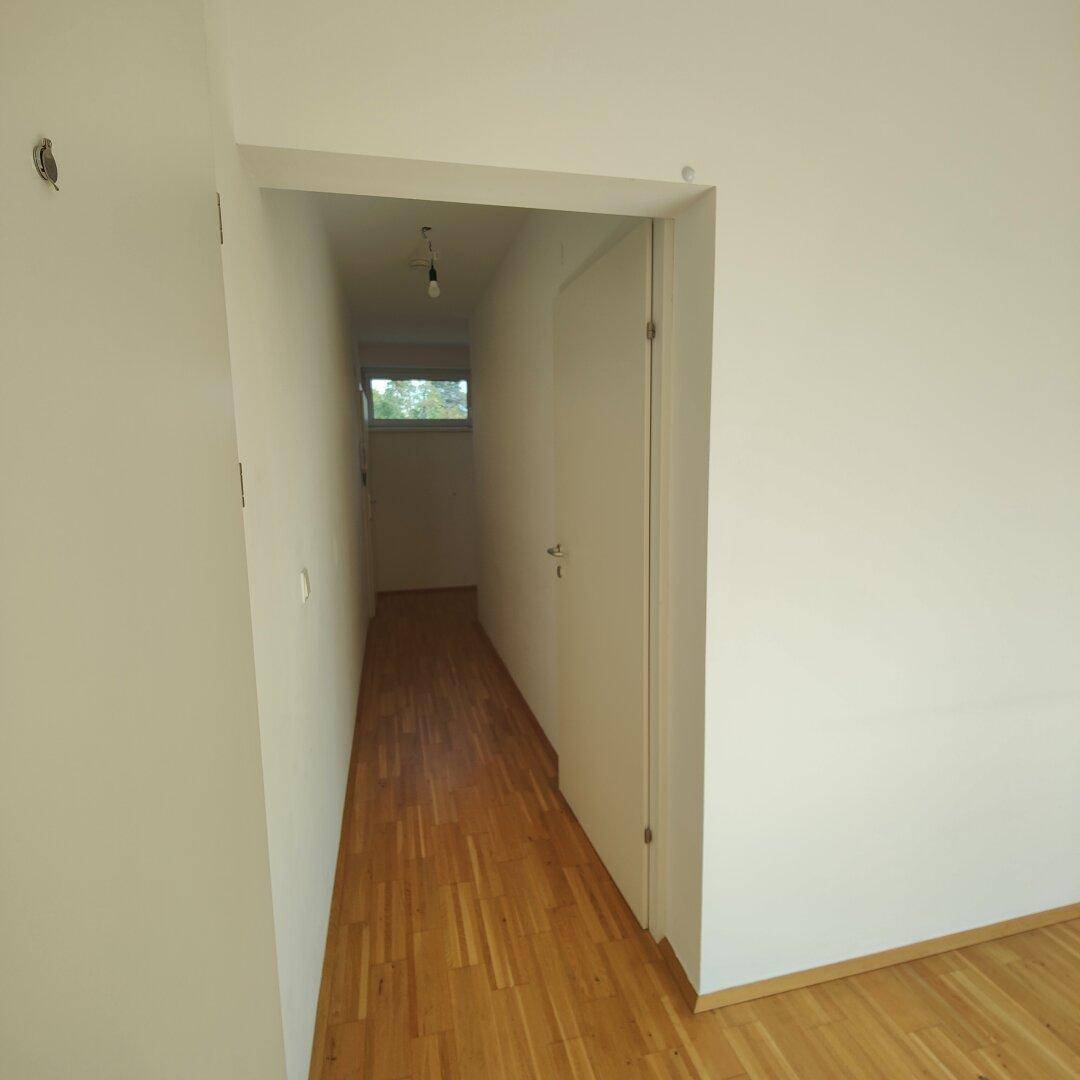 Langer, schmaler Flur mit Holzboden und einem Fenster am Ende, das Tageslicht spendet.