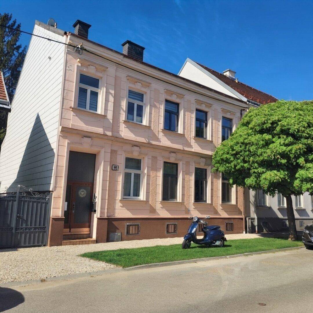 Historisches Gebäude mit beiger Fassade, großen Fenstern und einem modernen Anbau unter blauem Himmel.