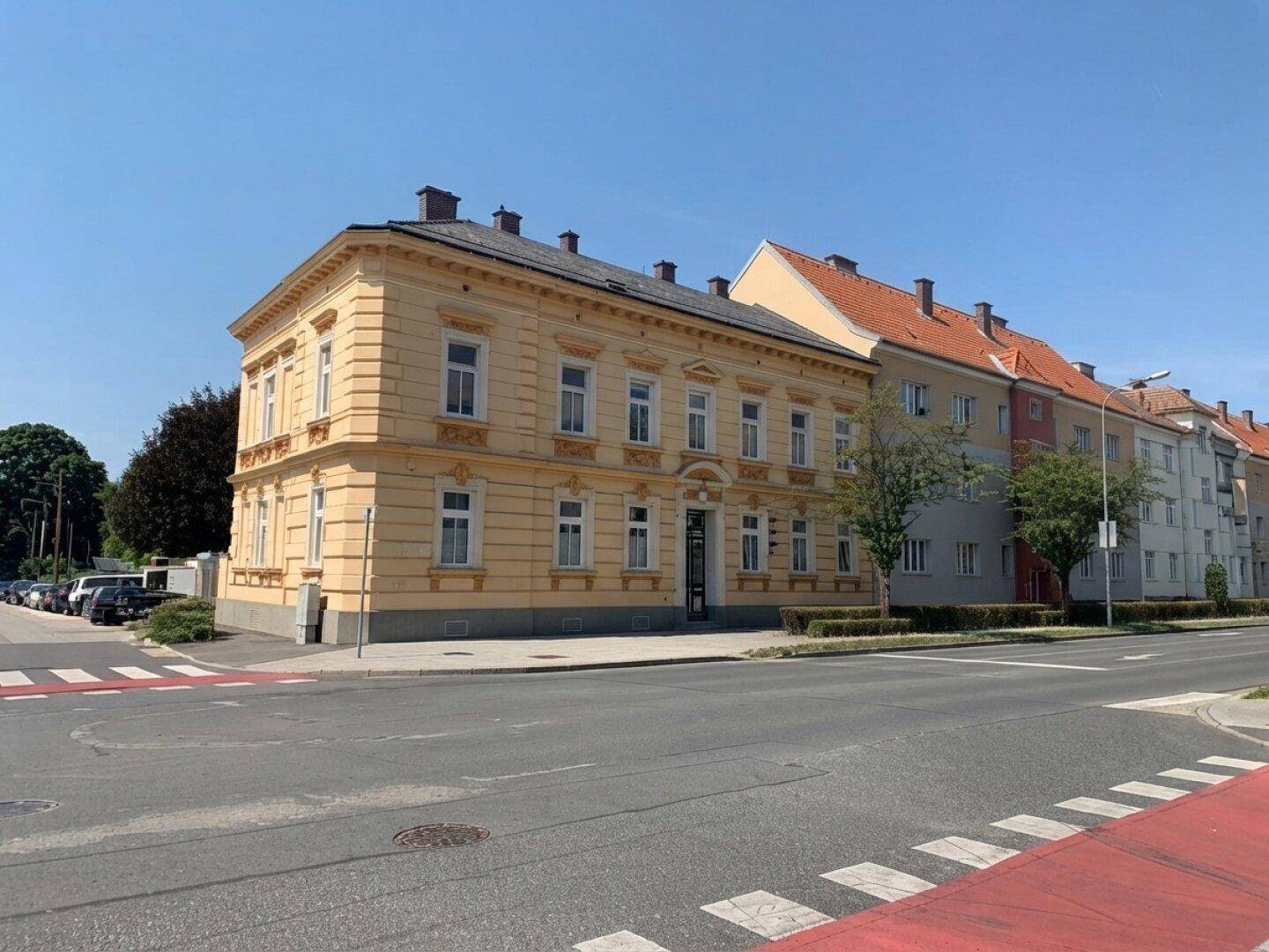 Weitwinkelansicht des charmanten gelben Gebäudes an einer Straßenecke mit angrenzenden Häusern und klarem Himmel.