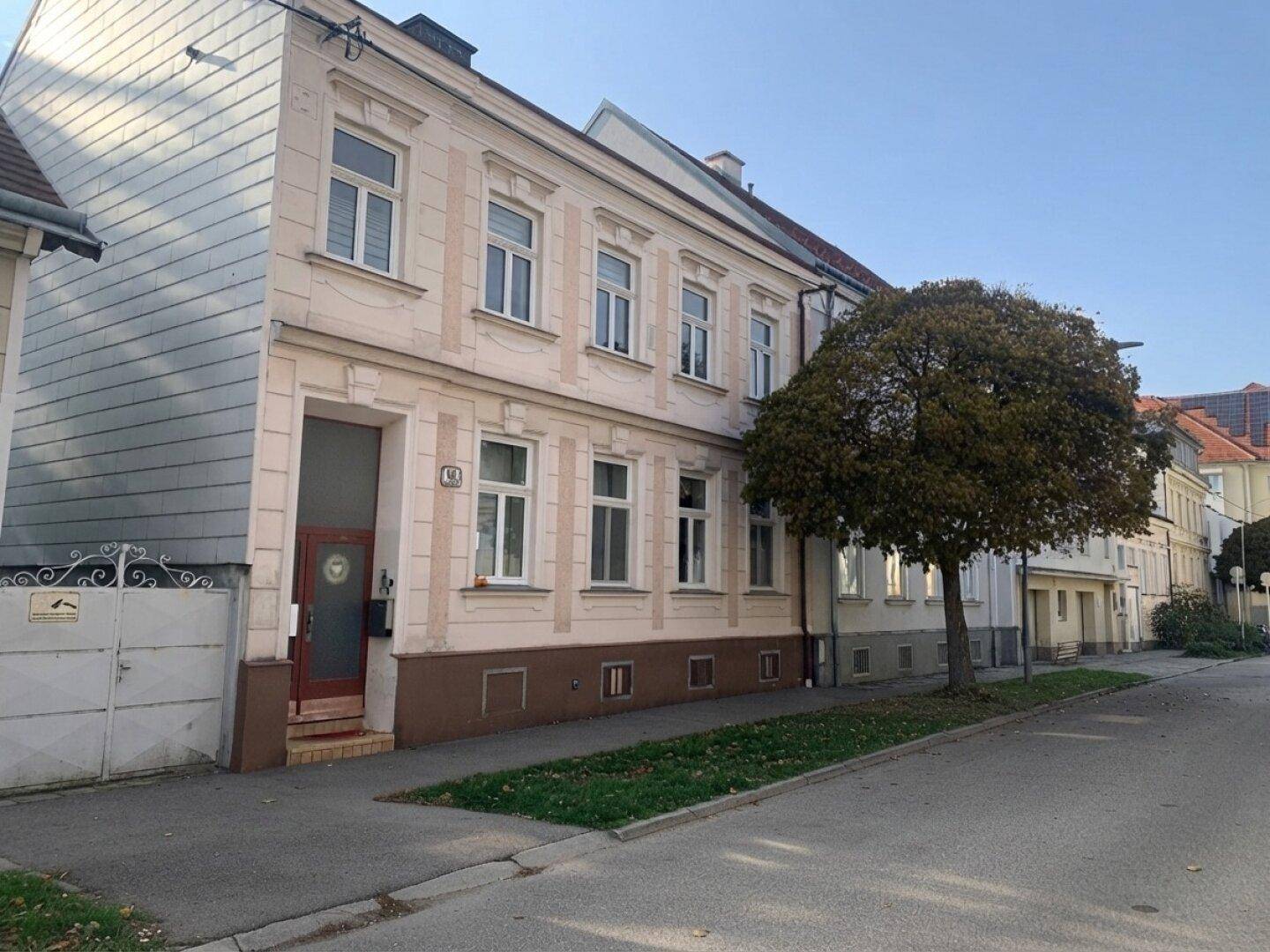Seitenansicht des Gebäudes mit beiger Fassade, vielen Fenstern und einem Baum davor.