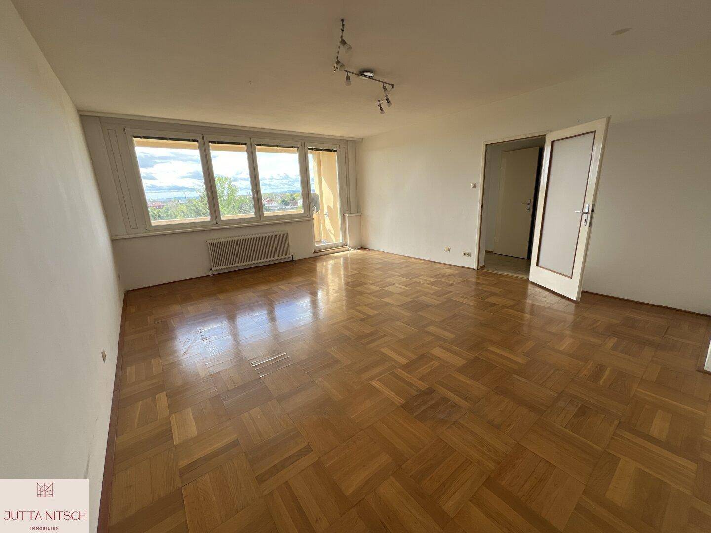 Helles Wohnzimmer mit Fischgrätparkettboden und Zugang zu einem Balkon.
