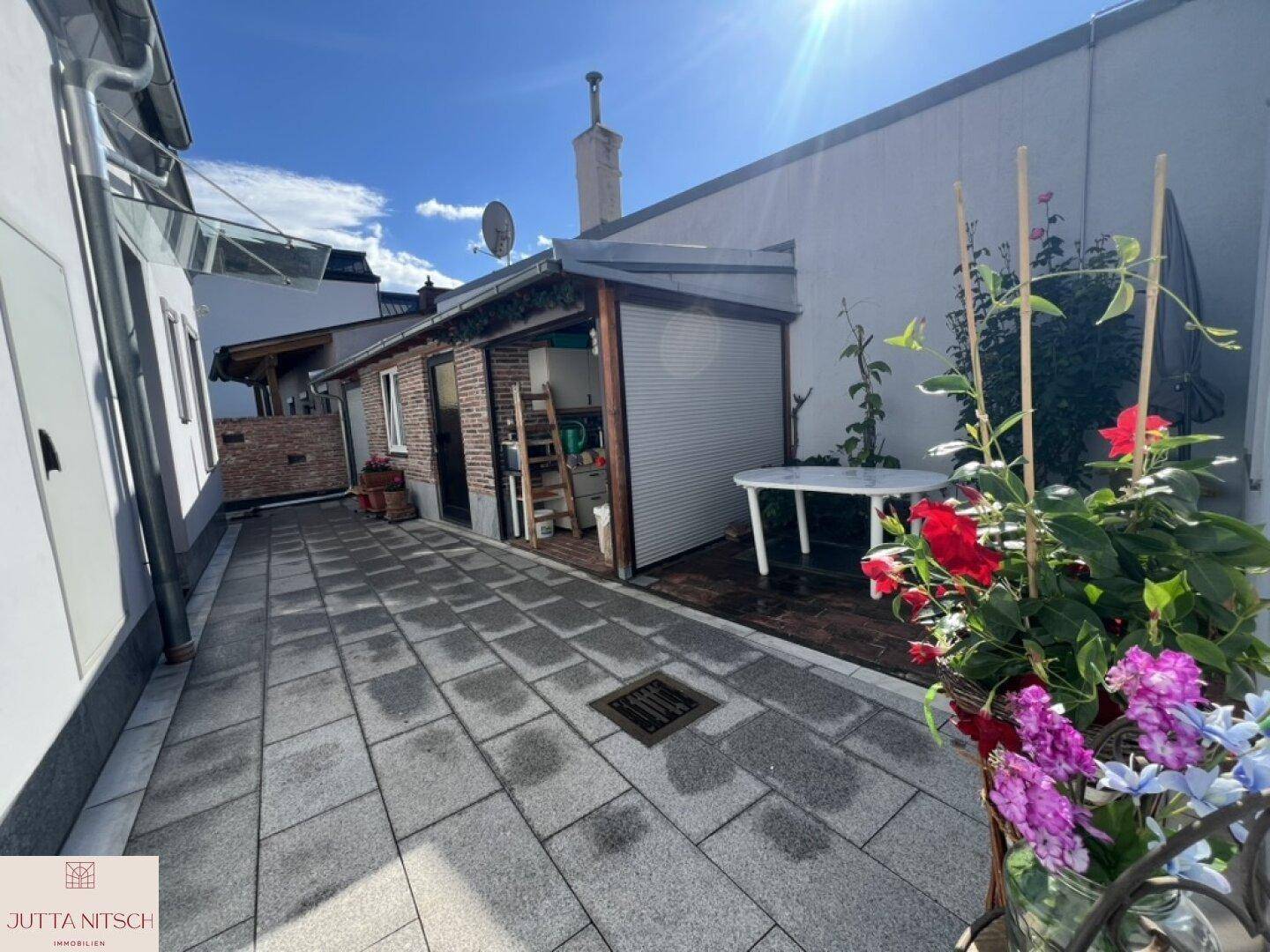 Sonniger gepflasterter Innenhof mit Sitzgelegenheit und Pflanzen.