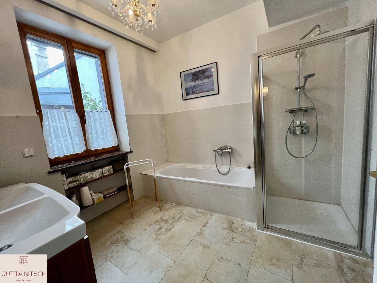 Badezimmer mit Badewanne, Duschkabine, Fenster und Fliesenboden.