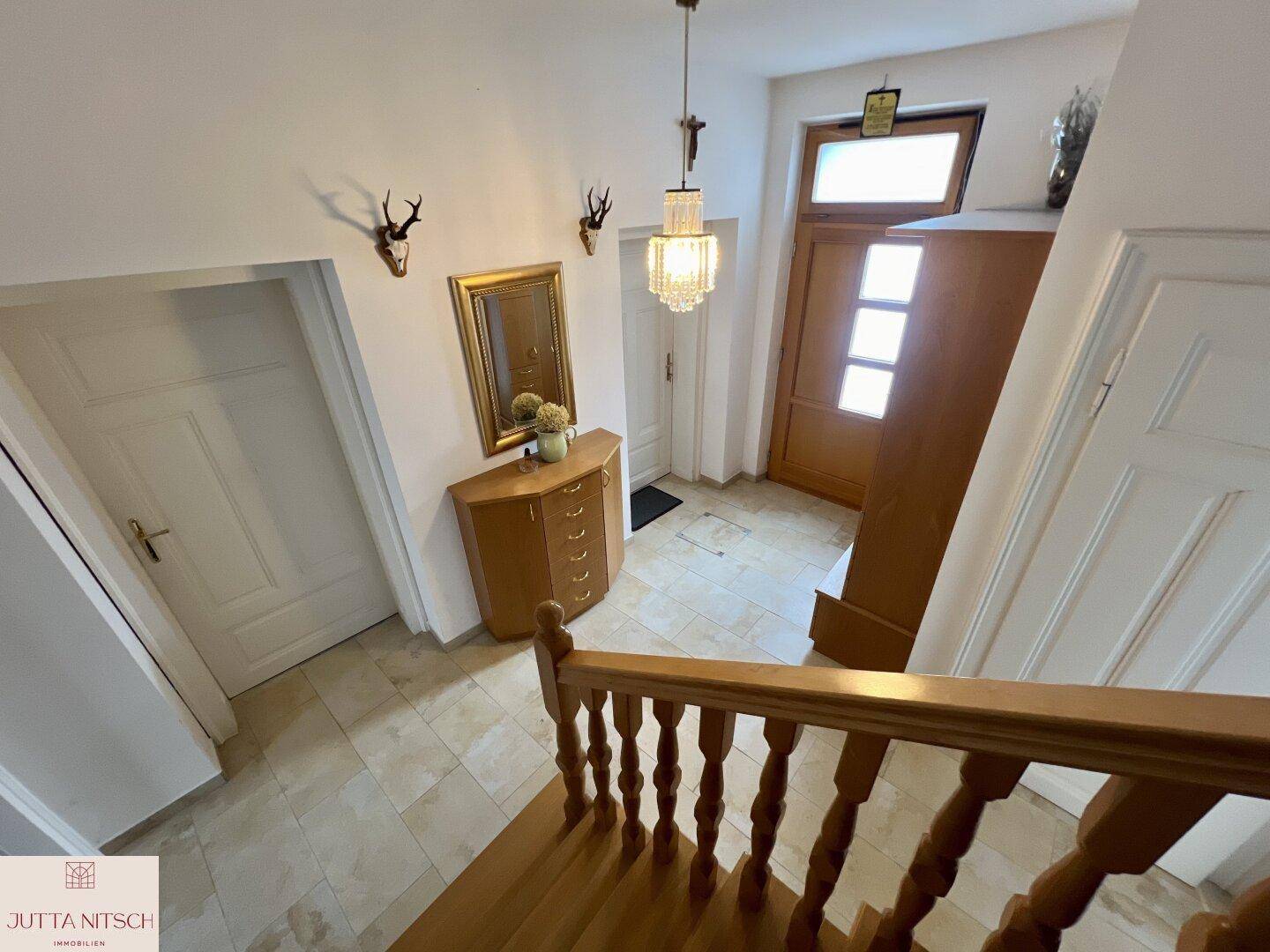 Heller Eingangsbereich mit Holztreppe, Fliesenboden und traditioneller Dekoration.