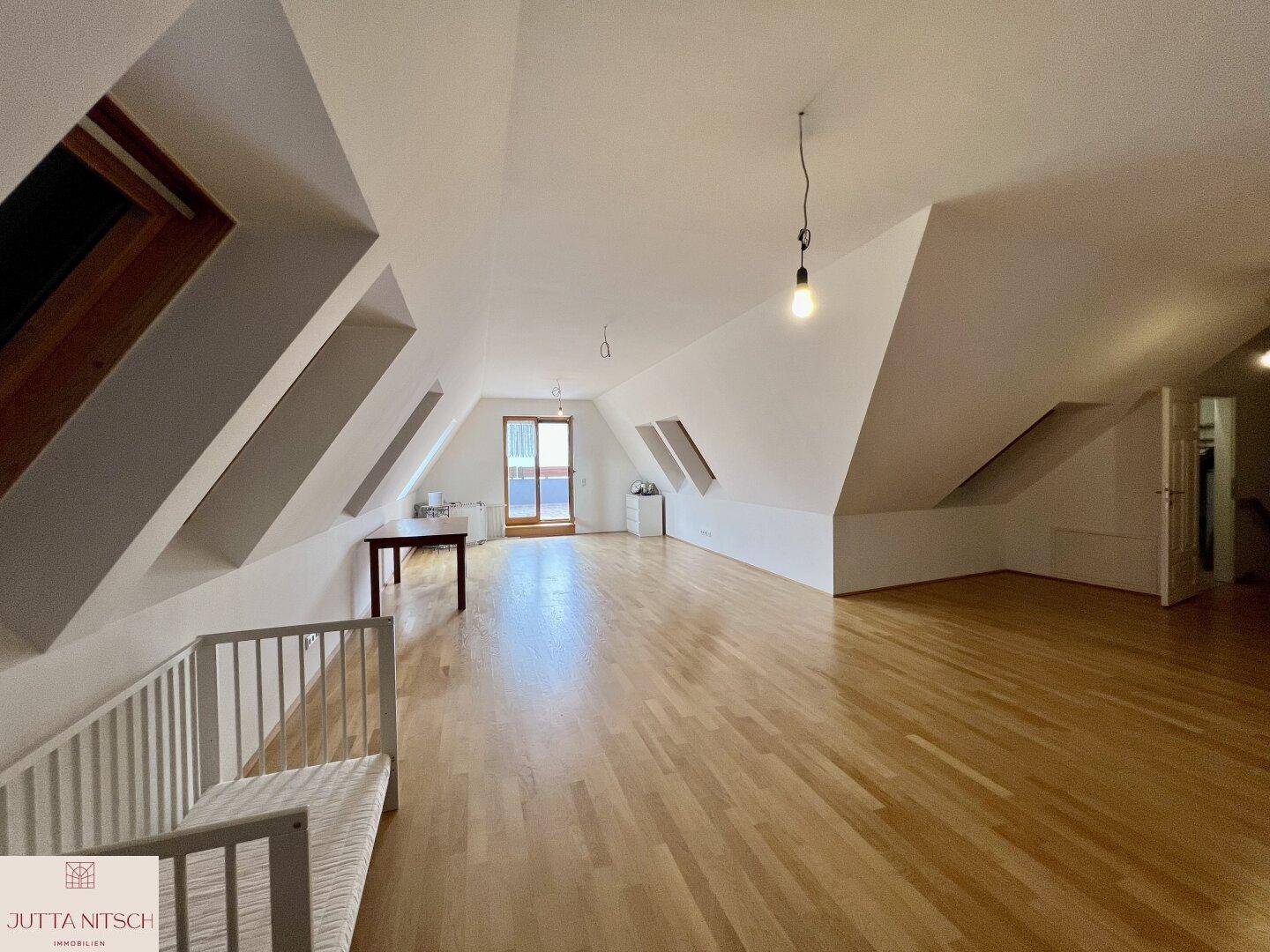 Geräumiger Dachbodenraum mit Holzboden, Dachschrägen und Zugang zu einem Balkon.