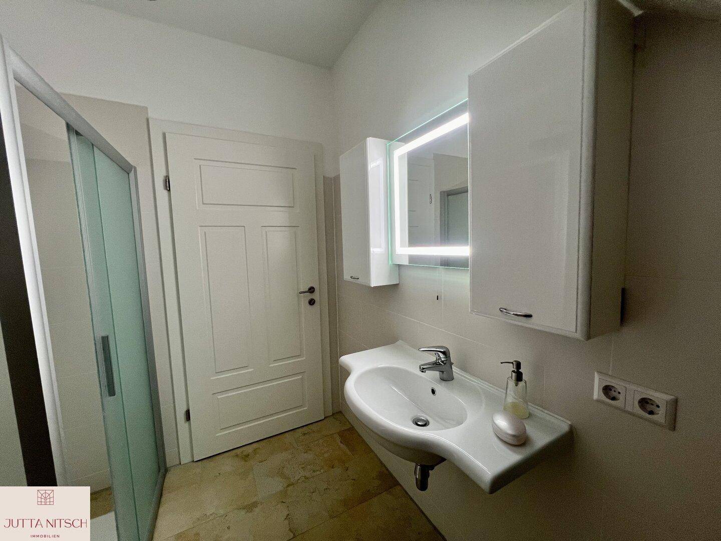 Modernes Badezimmer mit Waschtisch, beleuchtetem Spiegelschrank und Duschkabine.