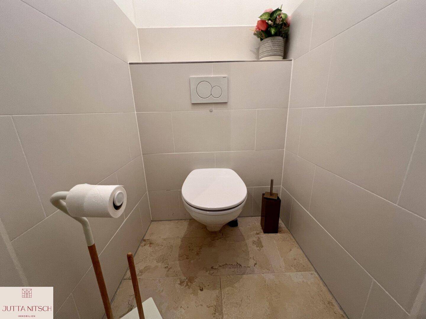 Separates WC mit Wand-WC, Fliesen und einfacher Dekoration.