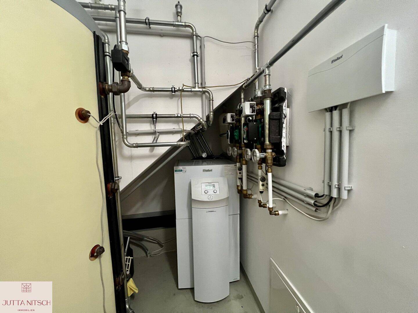 Technikraum mit Heizungsanlage, Warmwasserspeicher und sichtbaren Rohren.