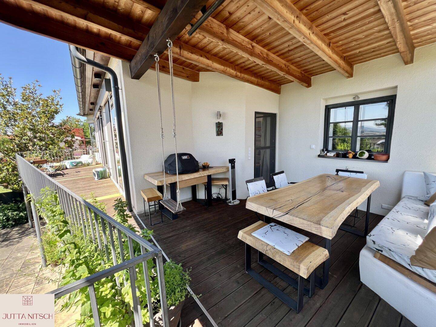 Geräumige überdachte Terrasse mit Holzdielenboden, Sitzgelegenheiten und weitem Blick ins Grüne.