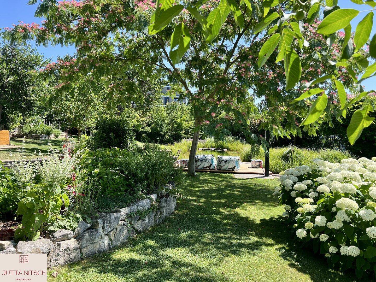 Weitläufiger Garten mit gepflegtem Rasen, schattenspendenden Bäumen und blühenden Sträuchern.