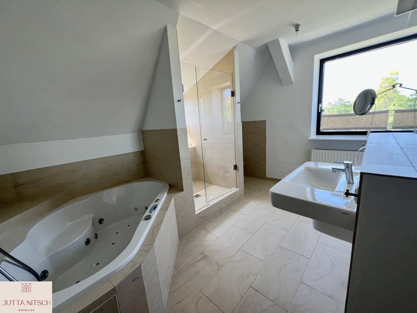 Helles Badezimmer mit Eckbadewanne, Glasdusche, Einzelwaschbecken und großem Fenster.