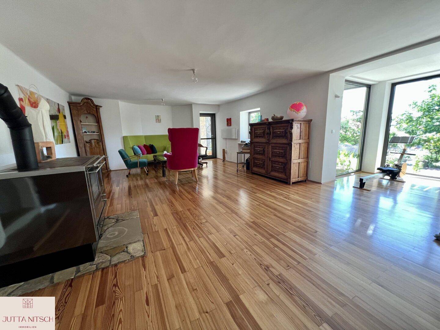 Geräumiges Wohnzimmer mit Holzboden, modernem Kaminofen und großen Fenstern mit Blick ins Grüne.